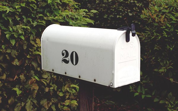 Weißer Briefkasten vor grüner Hecke