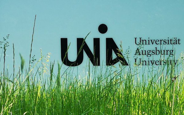 Universitäts-Logo, im Vordergrund ist eine Wiese zu sehen