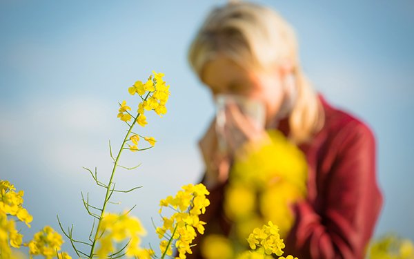 Frau mit Heuschnupfen steht neben Blumen