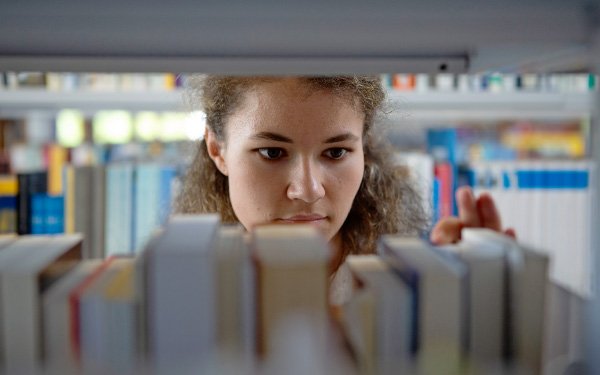 Blick durchs Bücherregal auf eine Studentin in der Bibliothek