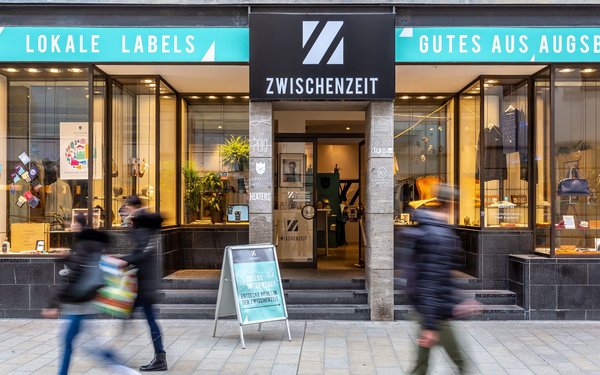 Bild des Ladens "Zwischenzeit" in der Augsburger Annastraße: Zu sehen ist die Schaufensterfront mit Passanten.