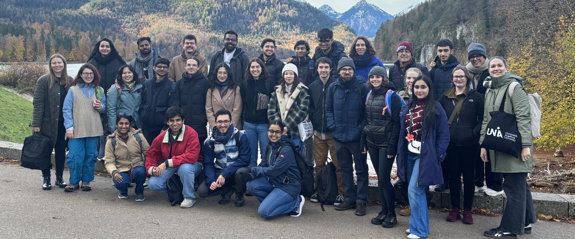 Group photo of international researchers in front of the lake, with a mountain panorama, at Neuschwanstein Castle