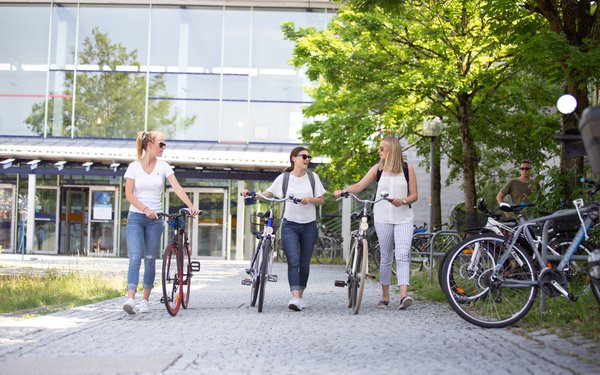Drei Studierende schieben Fahrräder vor dem Eingang des WiWi-Fakultätsgebäudes