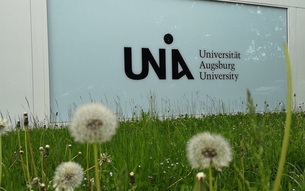 Gras und Blumen mit Uni-Logo am Y-Gebäude