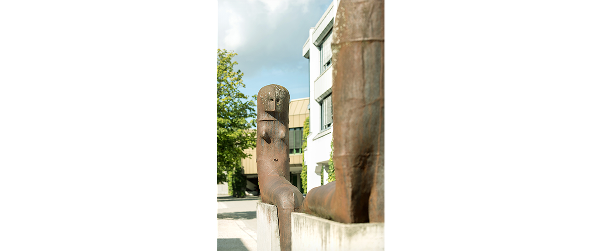 Auf dem Bild sieht man das Kunstwerk von Lothar Fischer, bei dem sich zwei Skulpturen gegenübersitzen auf Steinen.