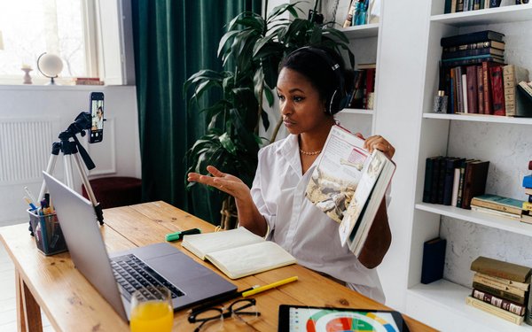 Eine Frau zeigt ein Buch vor ihrem Laptop