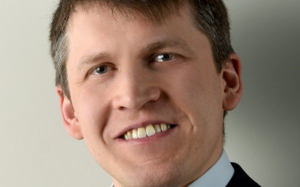 Porträtfoto von Dr. Jan Meier-Kolthoff. Er hat kurze, braune Haare, trägt ein hellblaues Hemd und eine schwarze Anzugjacke und lächelt in die Kamera.
