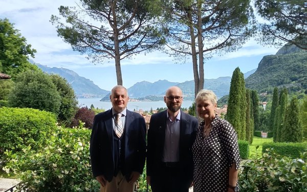 Drei Teilnehmende eines Workshops posieren in einem Garten mit Blick auf einen See und die Berglandschaft im Hintergrund