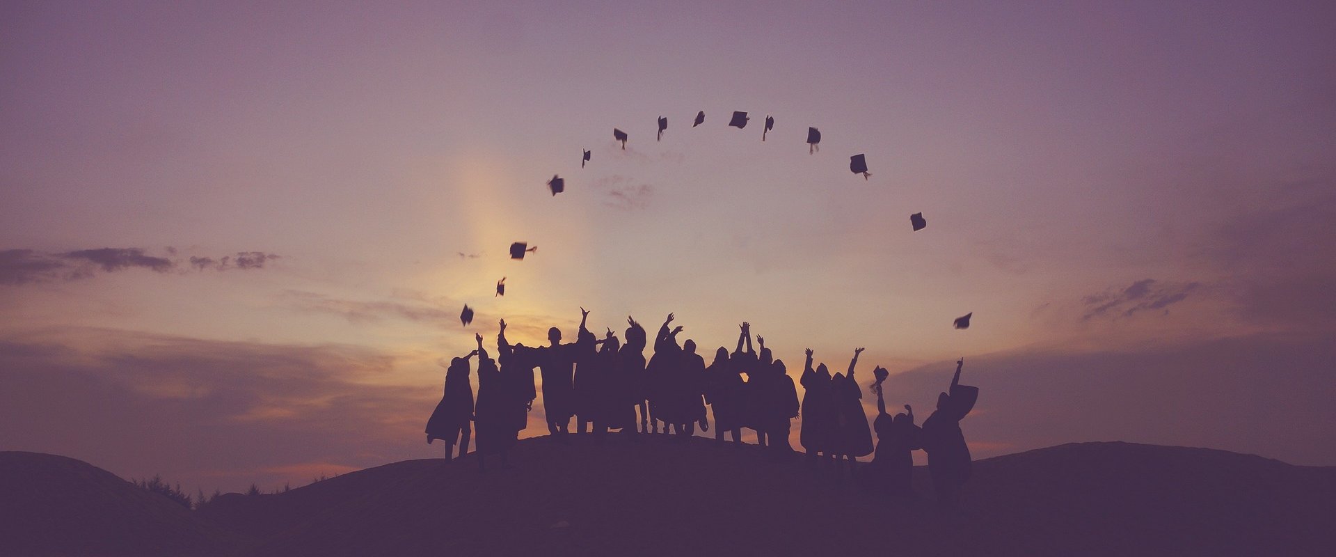Zeigt Graduierte, die ihren Hut im Sonnenuntergang hochwerfen.