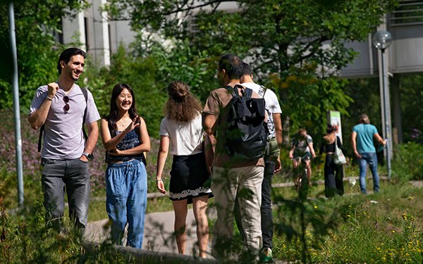 Studierende begegnen sich auf dem grünen Campus der Universität