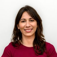 Frau mittleren Alters. Über schulterlange dunkelbraune Haare. Lächtelt. Trägt ein weinrotes Oberteil mit Rundausschnitt.