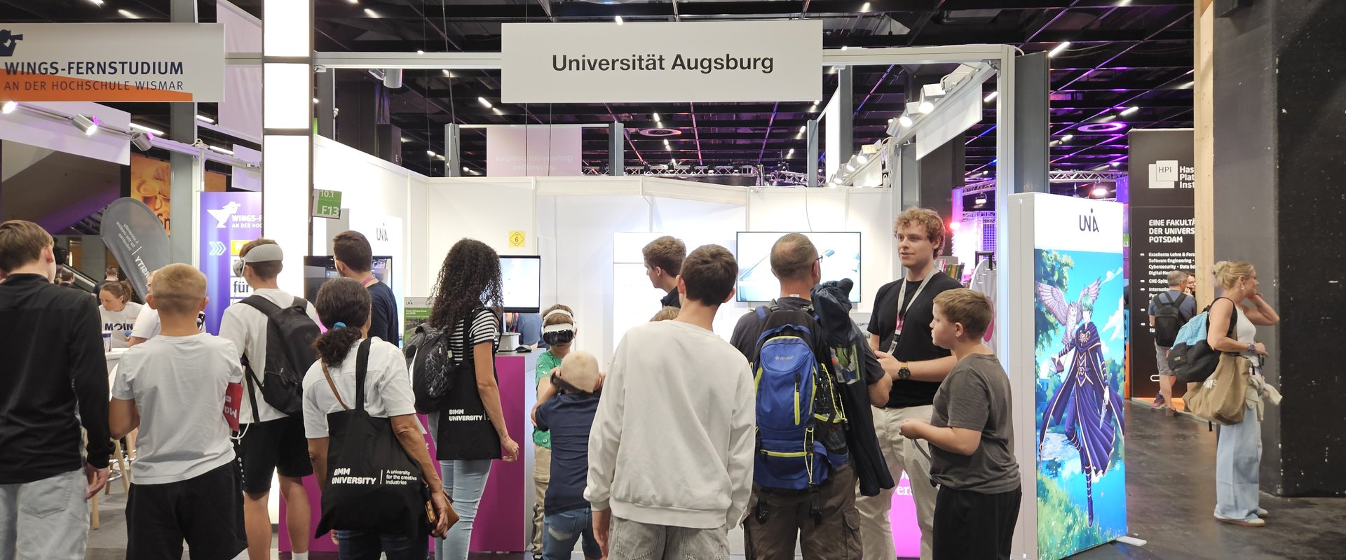 Many people can be seen from behind, crowding around the University of Augsburg stand.