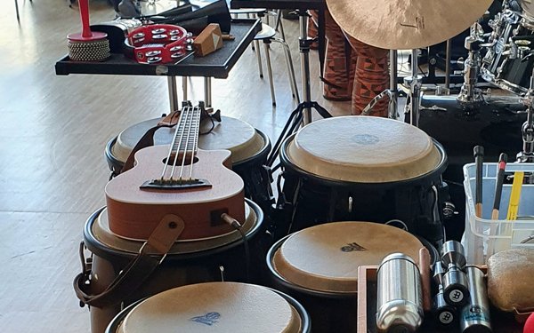 Eine Bass-Ukulele liegt spielbereit zwischen mehreren Congas und weiteren Rhythmusinstrumenten.