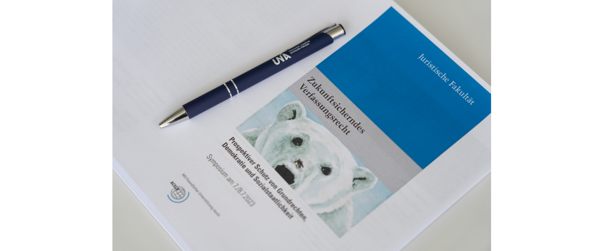 Unterlagen zum Symposium "Zukunftsicherndes Verfassungsrecht" am 7. und 8.7.2023: Veranstaltungsprogramm und Kugelschreiber der Universität Augsburg