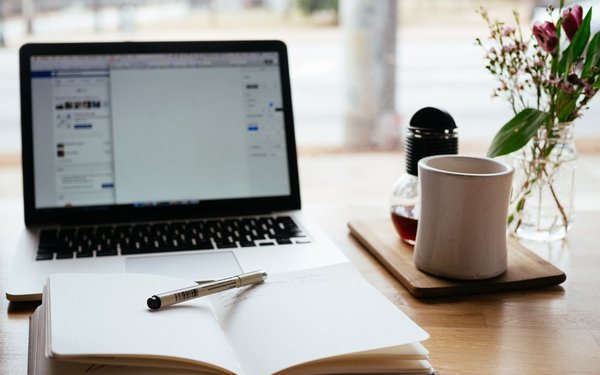 Schreibtisch mit offenem Buch und Computer im Hintergrund