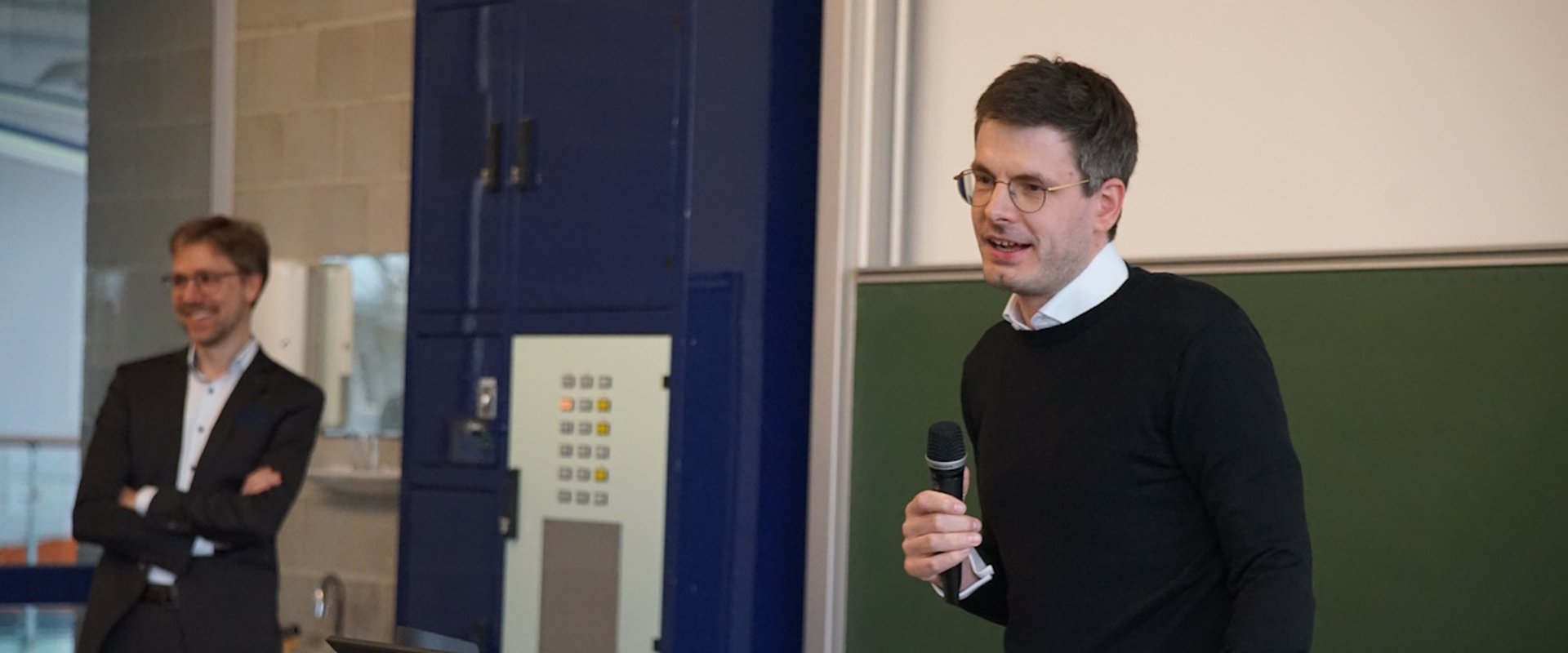 Dr. Eike Hosemann hält einen Vortrag. Im Hintergrund ist Prof. Lutzi zu sehen.