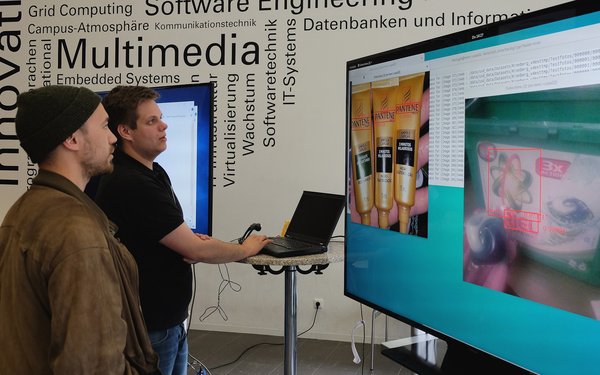 Zwei Menschen informieren sich an einem Stand mit großem Bildschirm