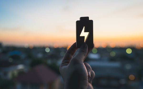 Vordergrund: Hand mit einem Batterie-Symbol, Hintergrund Abendhimmel