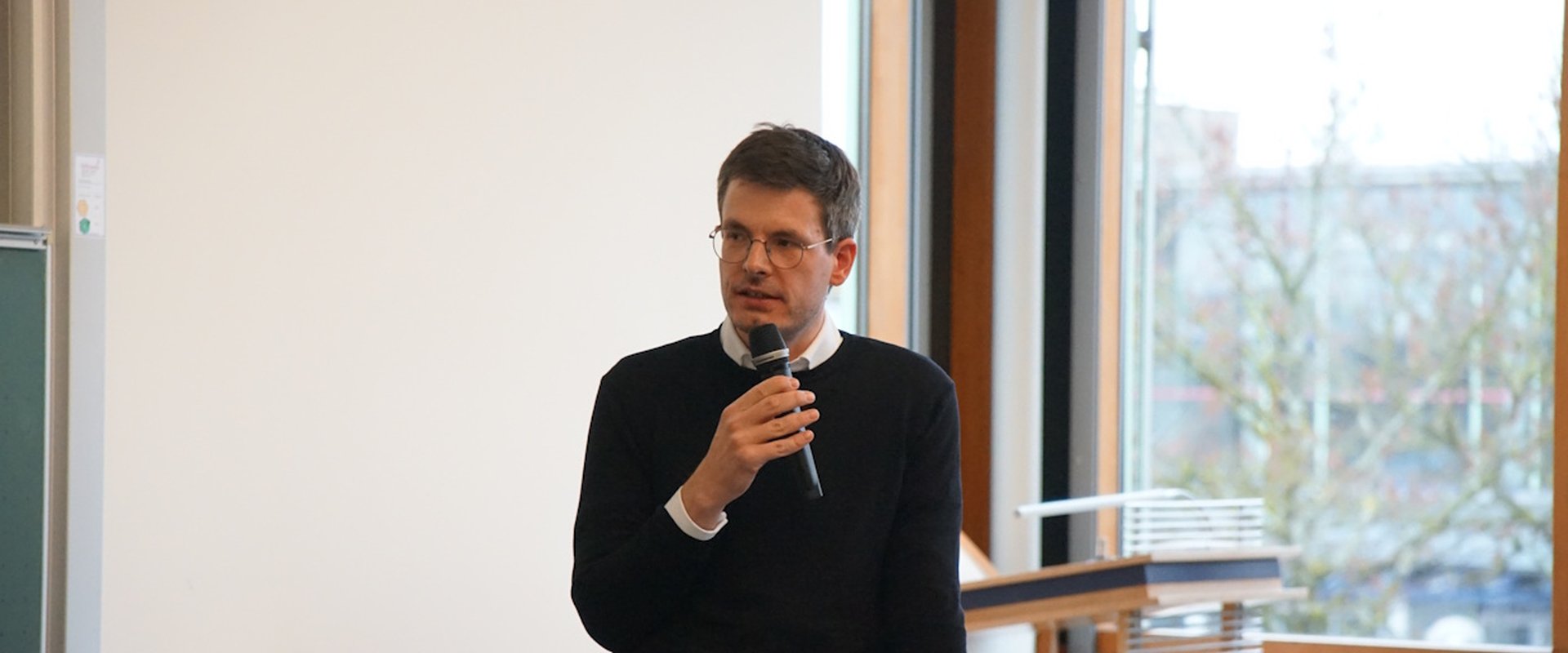 Dr. Eike Hosemann hält ein Mikrofon in der Hand und hält einen Vortrag.