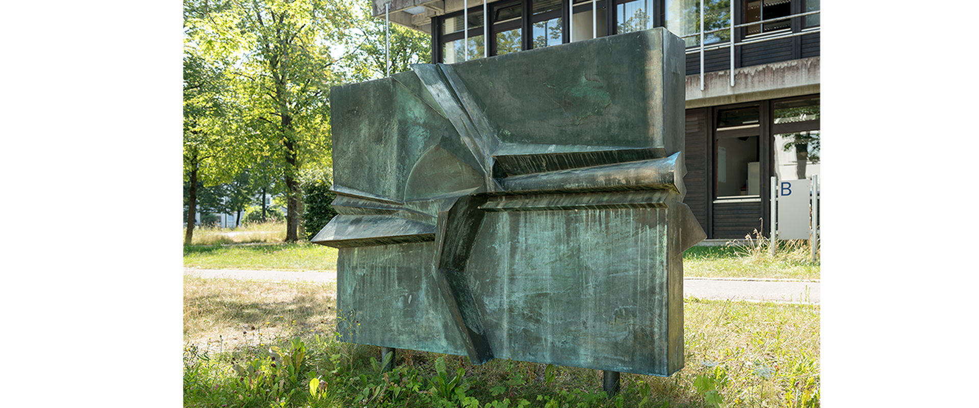 Das Kunstwerk Vogel beim Nestbau von Walter Schelenz, zeigt einen viereckigen Betonklotz, auf dem ein Reief hervorgehoben ist, welches den Schnabel eines Vogel erkkennen lässt.