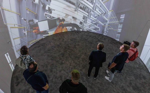 Das Bild zeigt Menschen im Dome des KUKA Gebäudes, auf den Wänden des runden Raumes läuft eine Präsentation.