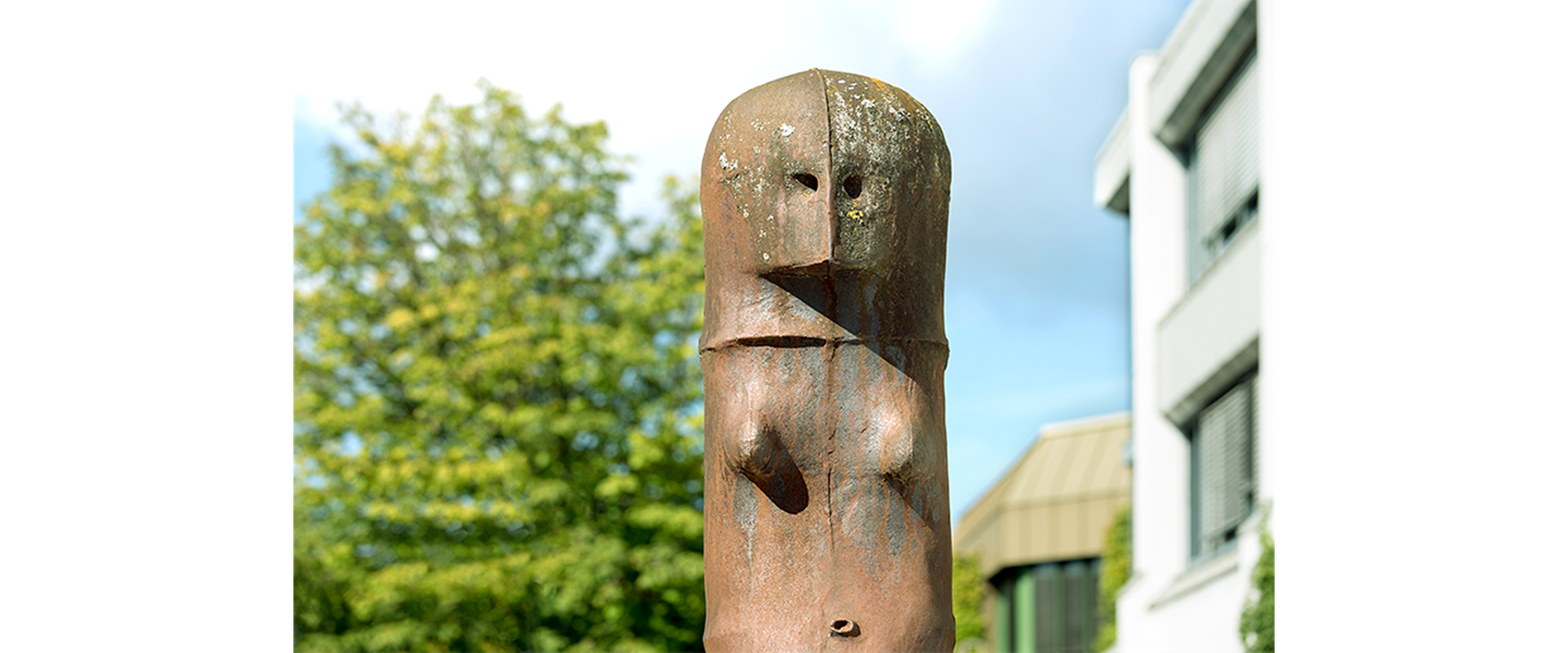 Auf dem Bild sieht man das Kunstwerk von Lothar Fischer, bei dem sich zwei Skulpturen gegenübersitzen auf Steinen.
