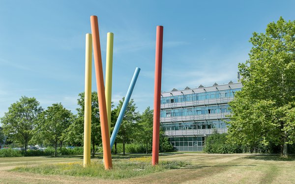 Auf dem Bild erkennt man das Kunstwerk Mikado von Edgar Knoop, auf dem bunte Metallstellen auf einem Rasen stehen.