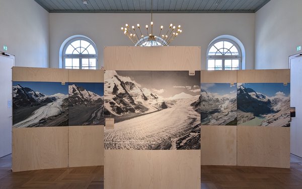 In einem Museumsraum stehen drei Holz e?nde auf die ein Bergpanorama gedruckt sind