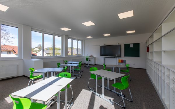 Sechs Tische mit grünen Stühlen stehen in einem Klassenzimmer.