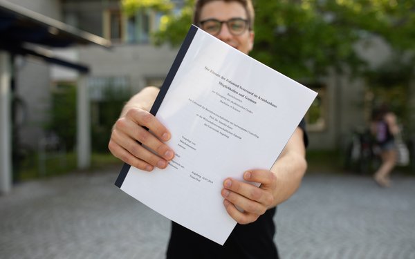 Student mit Bachelorarbeit in der Hand