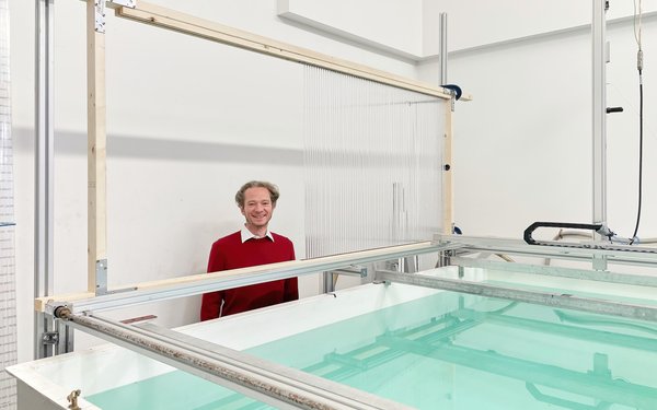 Prof. Dr. Malte Peter steht in rotem Pullover hinter einem Holzrahmen und einem Becken mit hellgrünem Wasser.