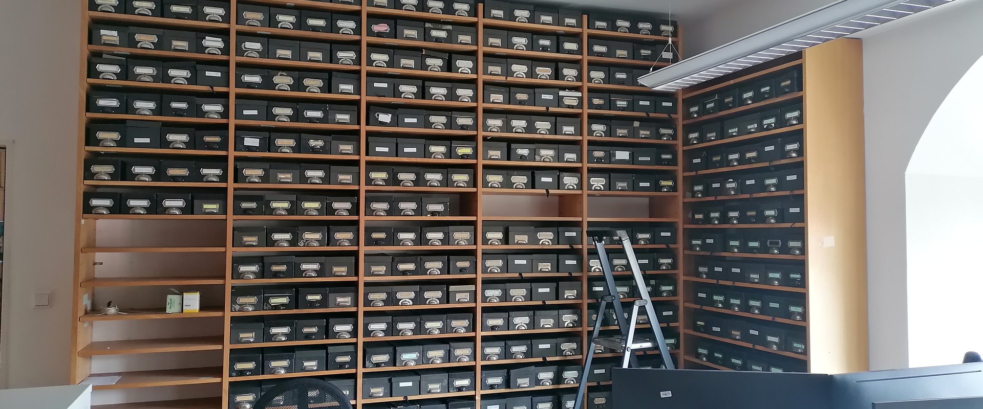 Auf dem Bild ist eine Wand des DIBS-Büro zu sehen, die voller Karteikästen ist.