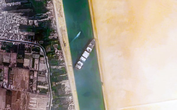 Das Bild wurde von oben aufgenommen und zeigt den Suez-Kanal, welcher von einem Frachtschiff blockiert wird.