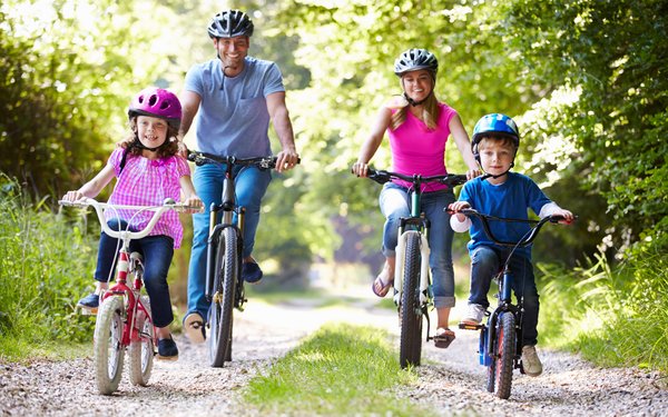 Mutter, Vater und zwei Kinder fahren auf einem Waldweg Fahrrad.