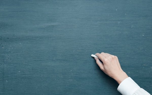 Hand hält Kreide und schreibt an Tafel