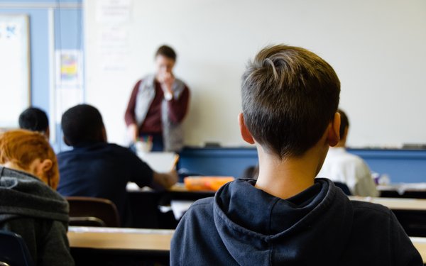 Im Vordergrund Schüler von hinten, im Hintergrund ist unscharf ein Lehrer zu sehen