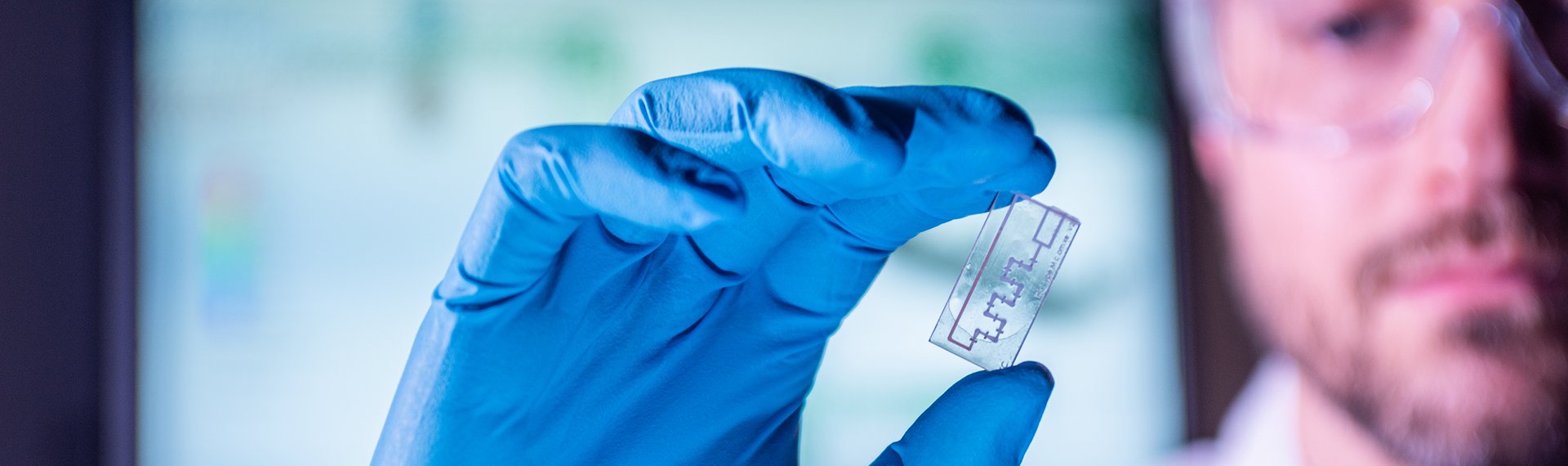 Wissenschaftler hält einen Chip in der Hand und trägt eine Schutzbrille und Schutzhandschuhe