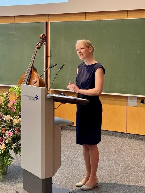 Professorin Dr. Verina Wild steht hinter einem Rednerpult, neben ihr Blumen.