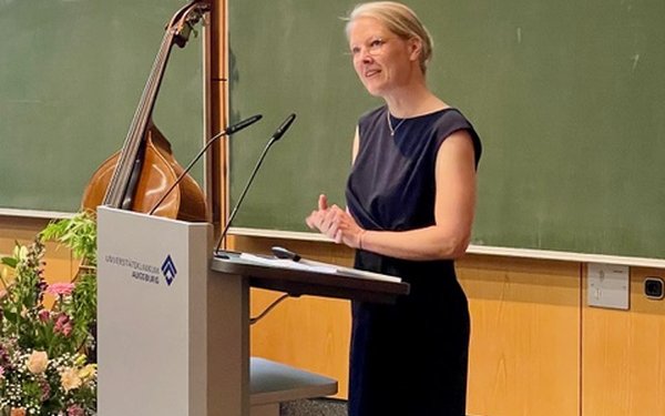 Professorin Dr. Verina Wild steht hinter einem Rednerpult, neben ihr Blumen.