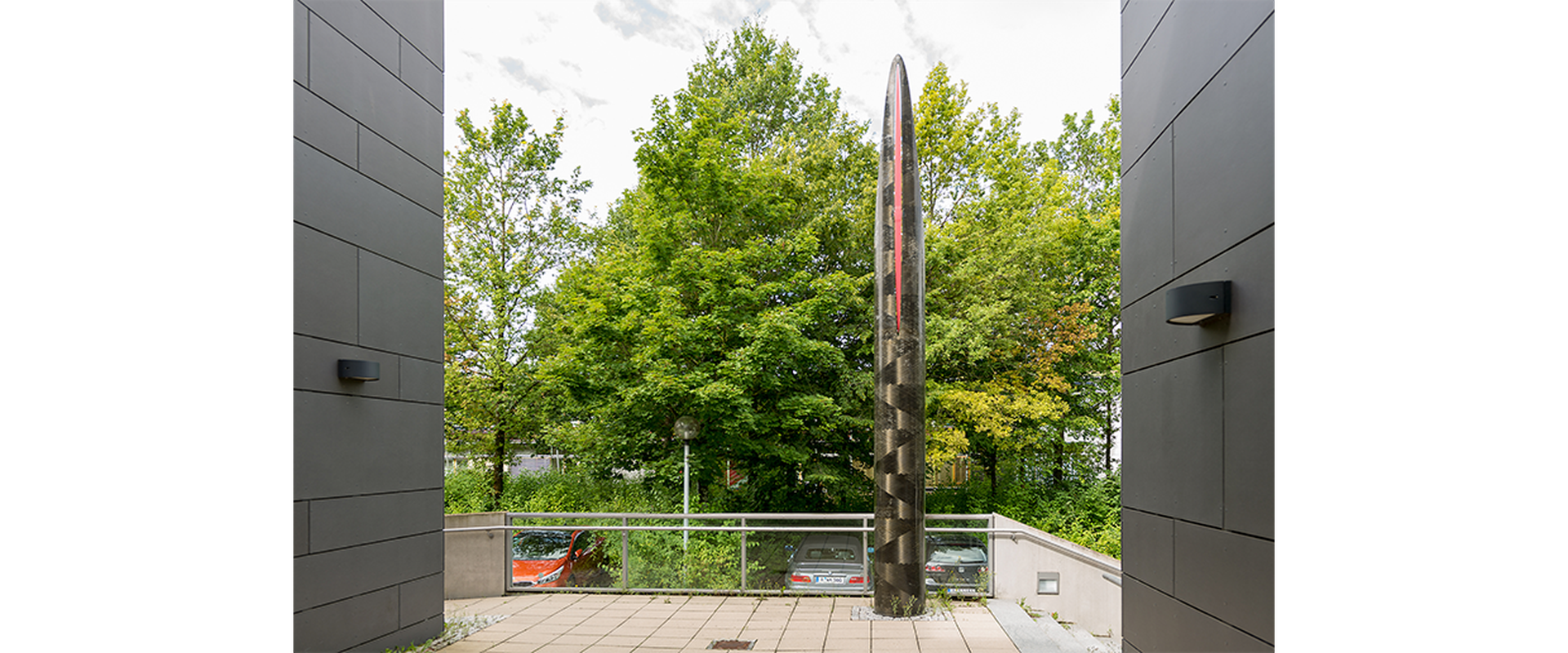 Auf dem Bild sieht man das Kunstwerk Pip vom Künstler Robert Kessler. Es stellt eine silberene Säule, die nach oben spitz zuläuft, dar.