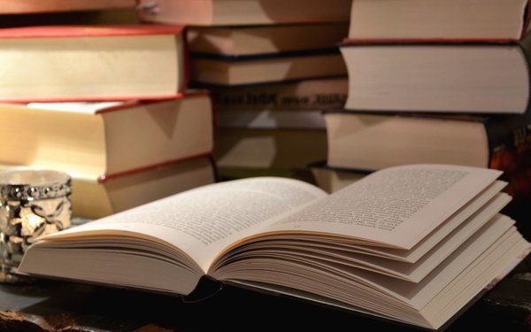 Aufgeschlagenes Buch und Bücher auf Schreibtisch