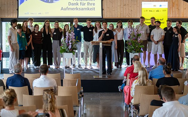 Gruppenfoto auf einer Bühne bei der KANU-Abschlussveranstaltung 2026; im Vordergrund sitzt das Publikum.