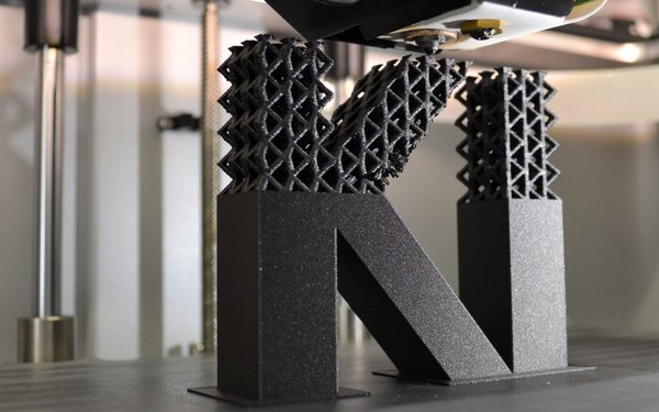Die Buchstaben KI, von einem 3D-Drucker generiert in einer entsprechenden Maschine als Symbol für das Thema.