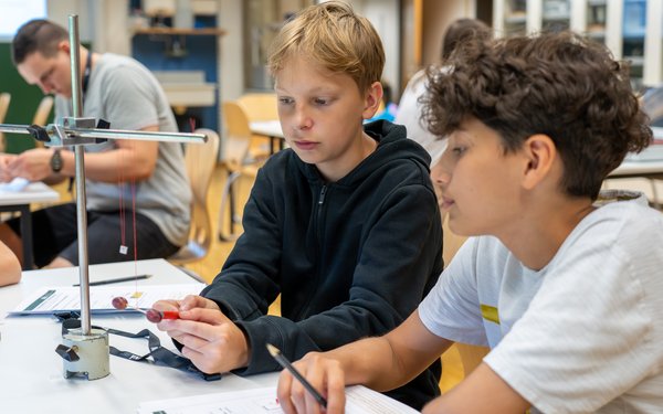 Zwei Schüler sitzen in einem Klassenraum und blicken auf einen Versuch mit zwei Weintrauben, der ihnen den Diamagnetismus näher bringt.