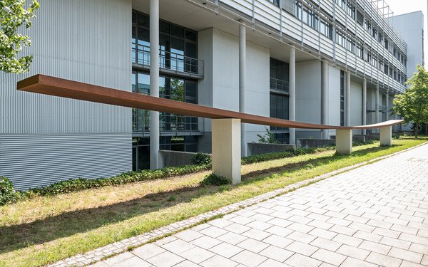 Auf dem Bild sieht man das Kunstwerk Stahlband, liegend auf drei Betonstützten von Hermann Kleinknecht