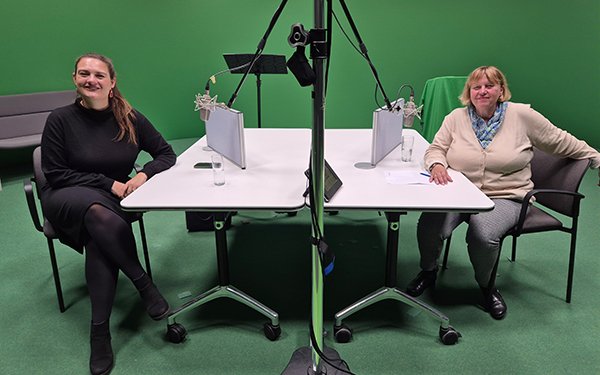 Die Journalistin Marlen Bruckner (links) und die Universit?tspr?sidentin Prof. Dr. Sabine Doering-Manteuffel (rechts) sitzen vor gr��ner Wand an einem wei?en Tisch, in der Mitte Mikrofone.