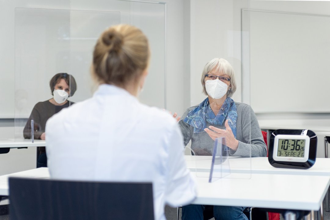 Studentin im Gespräch mit Schauspielpatientin, beobachtet von Prüferin
