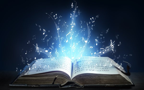 Ein altes geöffnetes Buch mit Notenschrift in einem dunklen Raum. Aus dem geöffneten Buch kommt wie durch Magie ein helles Licht und verschiedene Noten und Musiksymbole heraus.