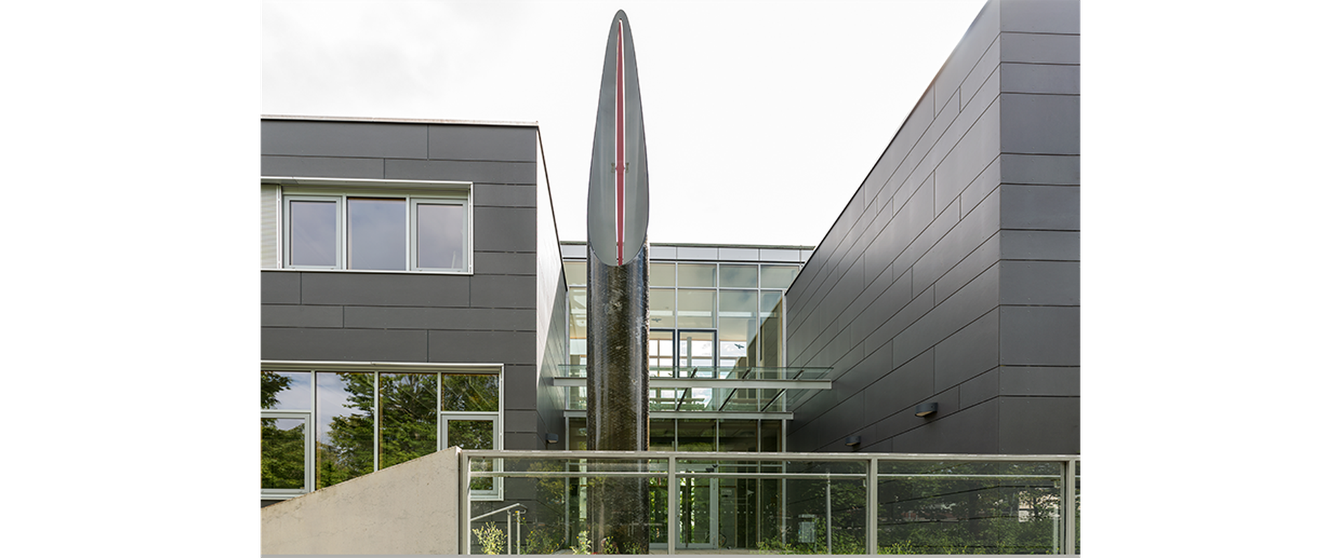 Auf dem Bild sieht man das Kunstwerk Pip vom Künstler Robert Kessler. Es stellt eine silberene Säule, die nach oben spitz zuläuft, dar.