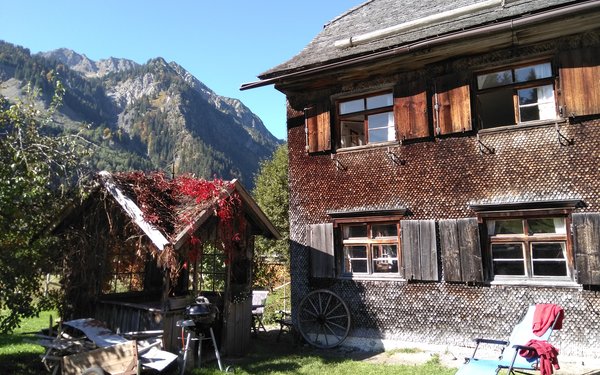 Blick auf die Unterkunft, ein historisches Allgäuer Bauernhaus, mit Gartenlaube, im Hintergrund die Allgäuer Alpen